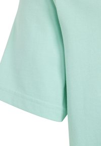 Detail mintově zeleného bavlněného trička s hladkou texturou, krátkým rukávem a pečlivě šitou lemovkou. Jednoduchý design bez dalších vzorů.