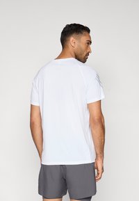 Bílé sportovní tričko s krátkými rukávy, hladkou texturou a kulatým výstřihem; má jemné šedé detaily na ramenou a zádech.