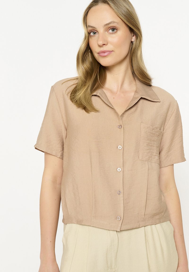 Short-sleeve, collared shirt in beige fabric with a textured finish, featuring a pocket and button closure along the front.