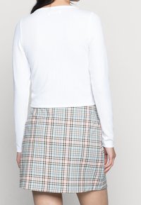 Bílý žebrovaný top s dlouhým rukávem v kombinaci s mini sukní v kostkovaném vzoru, která obsahuje modrou, hnědou a růžovou barvu. Tkaniny jsou měkké a mají přiléhavý střih.