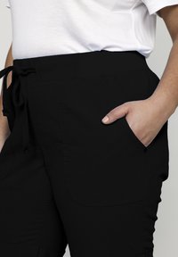 Black pants with an elastic waistband and drawstring, featuring side pockets and a smooth texture. Simple design, no visible patterns.