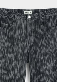 Pantalon en jean rayé noir et gris avec poches avant, passants pour ceinture et fermeture par un bouton blanc, étiquette "FRILIVIN" à l’intérieur de la ceinture.