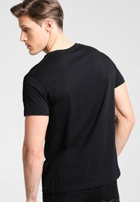 Black cotton crew neck t-shirt displayed from the back, featuring short sleeves and a simple, solid design without visible patterns.