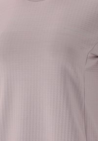 Lyslilla activewear skjorte lavet af struktureret stof, med rund halsudskæring og ordet "ENDURANCE" i lyseblå på forsiden.