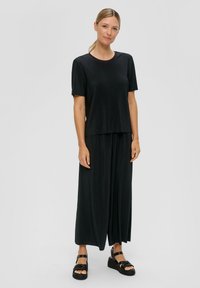 Czarna ribbed t-shirt z krótkim rękawem w połączeniu z luźnymi czarnymi spodniami. Strój charakteryzuje się swobodnym krojem i gładką fakturą, dopełniony masywnymi czarnymi sandałami.