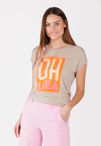 T-shirt beige à manches courtes avec un graphique audacieux "OH LALA" en orange et rose. Associé à un pantalon rose clair bien taillé. Texture lisse.