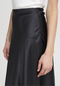 Mustat satiinihame, jossa on sileä rakenne ja korkea vyötärö. Sivuvetoketjuyksityiskohta on näkyvissä, mikä korostaa hoikkaa muotoilua.