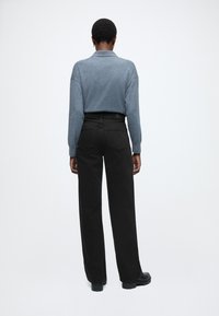 Tmavé široké nohavice v kombinácii s modrým voľným pleteným svetrom, pohľad zozadu. Hladká tkanina a minimálne detaily.