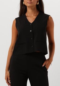 Chaleco sin mangas negro con escote en V, botones delanteros y dos bolsillos laterales. Fabricado en tejido suave con un diseño corto.