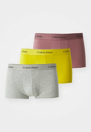 Drei Paar Calvin Klein Boxershorts in Grau, Gelb und Pink. Mit elastischen Taillengummis, auf denen der Markenname in Schwarz gedruckt ist.
