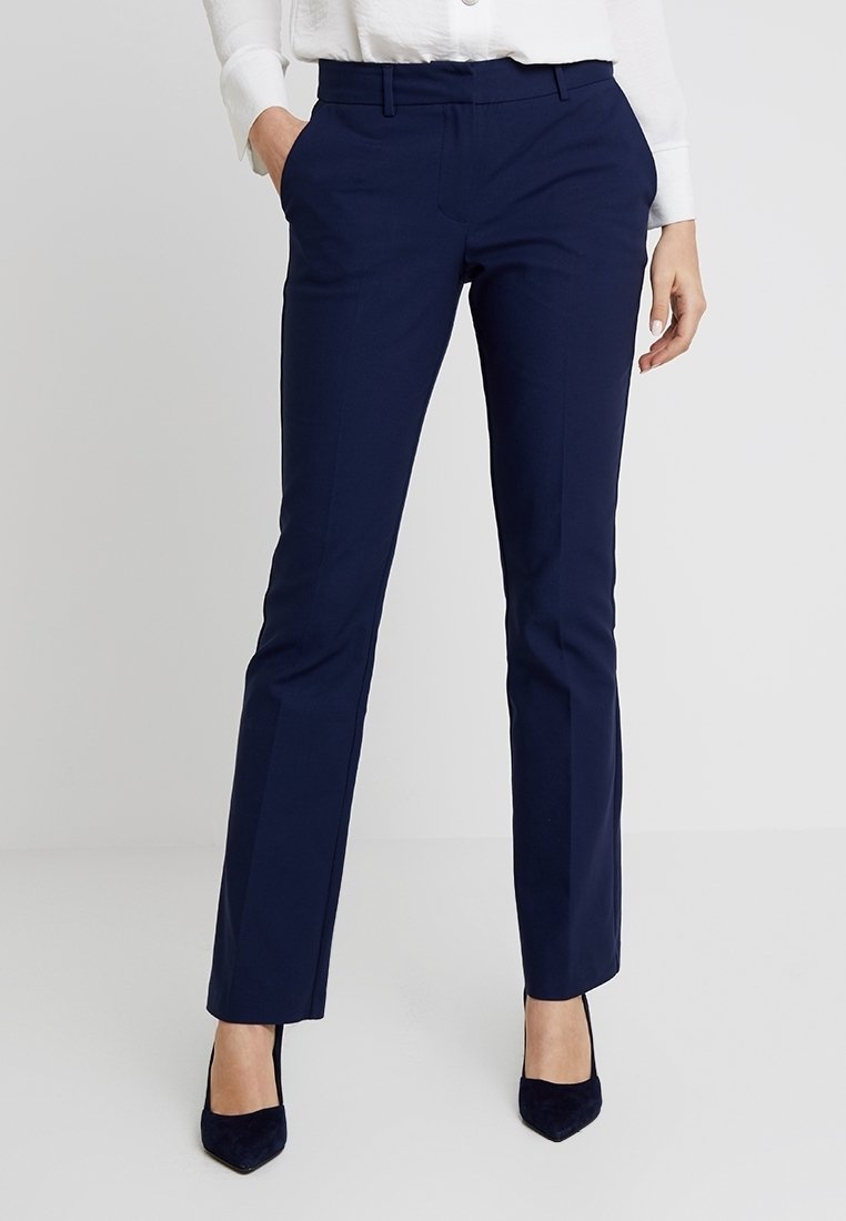 Pantalon sur mesure bleu marine à coupe droite, doté d'une texture lisse, de passants pour ceinture et de poches latérales, associé à des talons noirs pointus.
