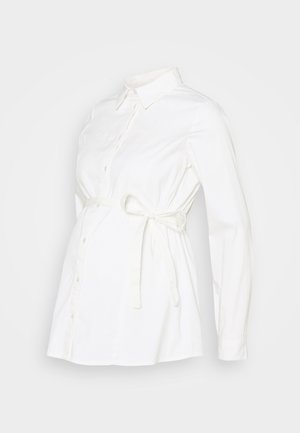 Biała koszula ciążowa z guzikami z przodu, długimi rękawami i wiązanym paskiem dla regulowanego dopasowania. Wykonana z miękkiego materiału o gładkiej fakturze.