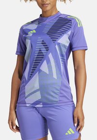 Maillot de sport et shorts violets avec des motifs géométriques et des accents verts. Fabriqués en matériau respirant avec une coupe ajustée.