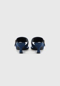 Talons ouverts en denim bleu foncé avec une finition texturée, présentant un petit talon épais et un accent doré sur le côté.