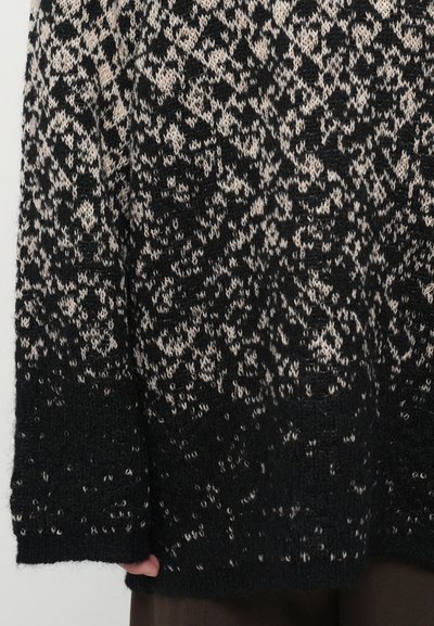 Black and beige knitted sweater with an abstract pattern, featuring a loose fit and textured fabric. Sleeve cuffs are ribbed.
