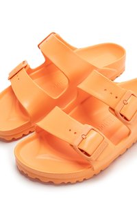 Chanclas de plástico naranja con dos correas ajustables, plantilla texturizada y una suela con patrón para mayor agarre. Ligeras y fáciles de limpiar.