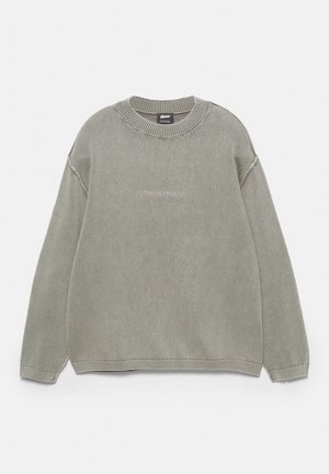 Lysegrå strikket rundhalset sweater med lange ærmer og diskret "Stwdstudio"-logo broderet på brystet.