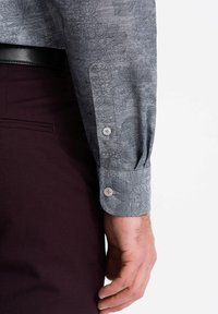 Camisa gris con estampado floral, detalles en los puños y dos botones, combinada con pantalones burdeos oscuros. Textura ligera y corte ajustado.