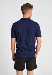 Mörkblå kortärmad pikétröja i följsam bomull, med en enkel krage och avslappnad passform, som bärs med svarta shorts.