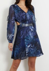 Robe à motif tropical avec un décolleté en V profond, des manches longues avec des liens, des côtés découpés et une large ceinture, dans des nuances de bleu et de vert.