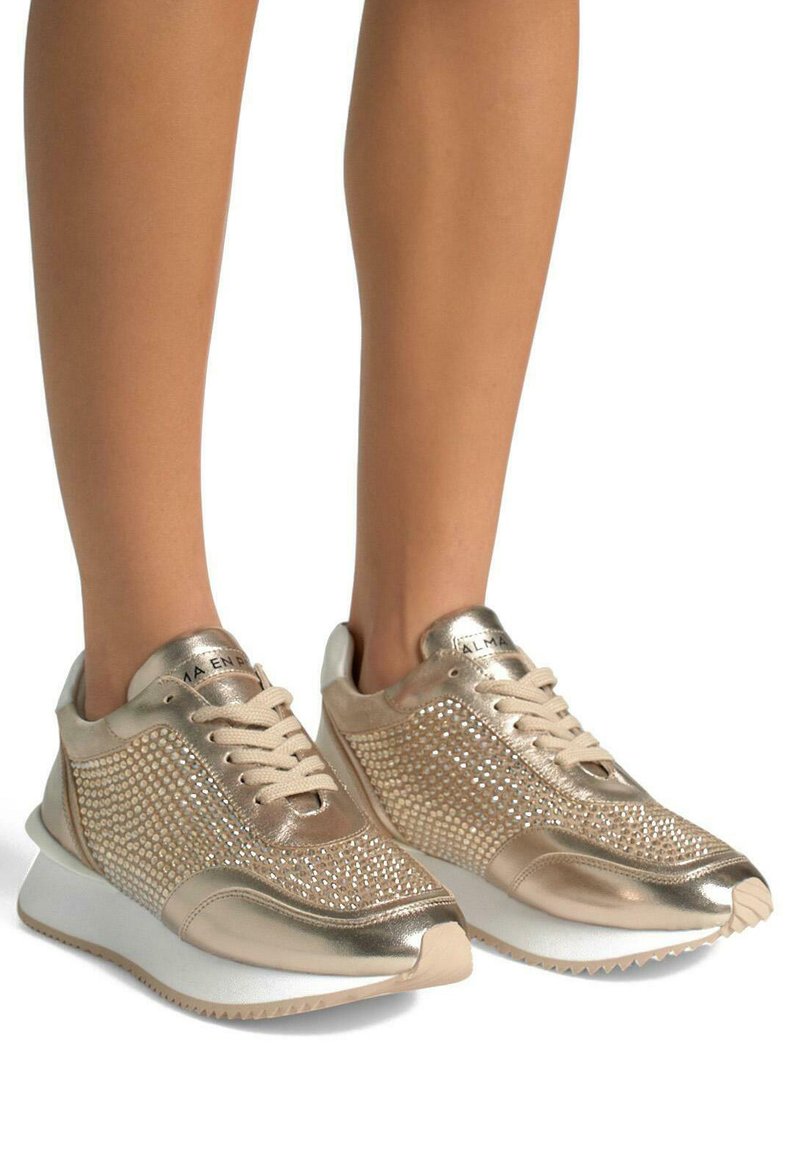 Sneakers metallici dorati con accenti luccicanti di strass, lati in mesh testurizzato e suola in gomma bianca. Design con lacci e dettaglio del logo.