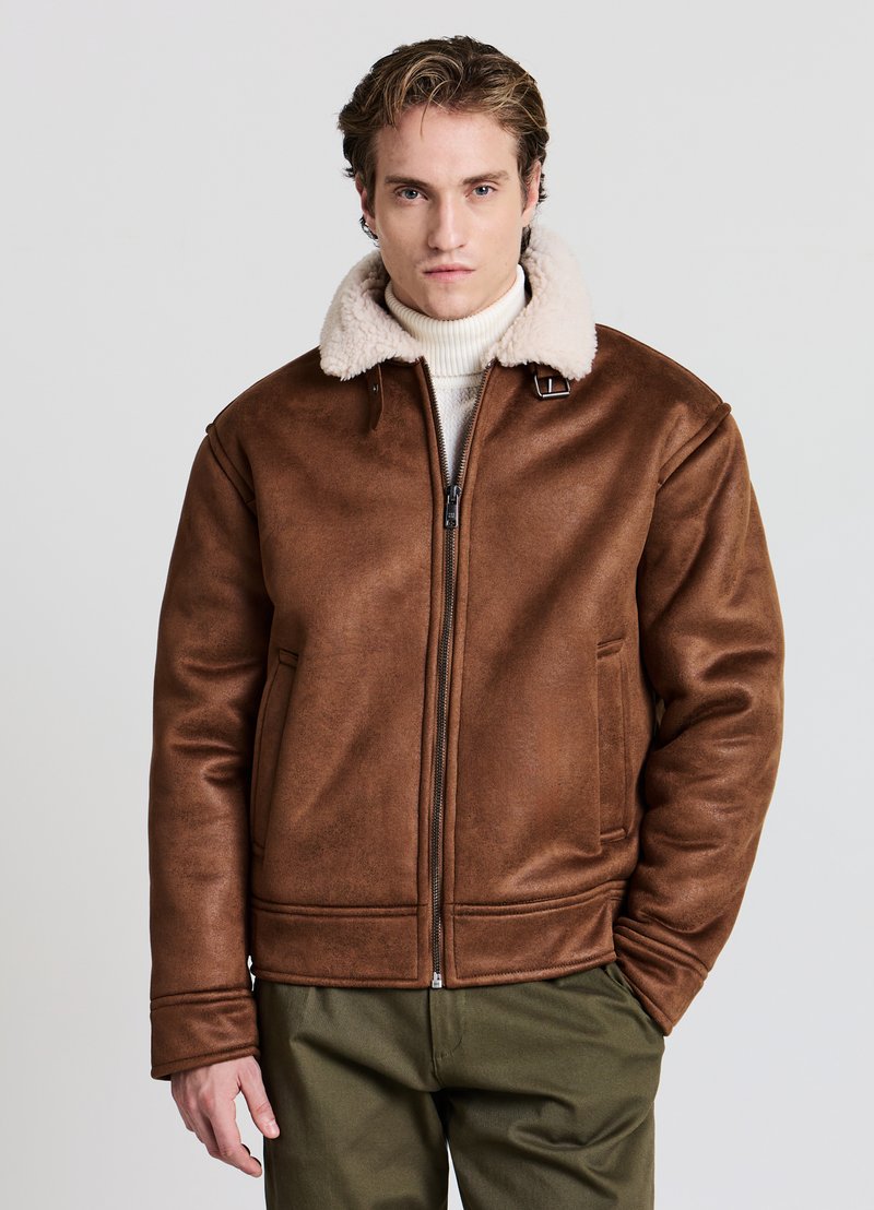 Giacca marrone in ecopelle con colletto in shearling crema, chiusura frontale con cerniera e due tasche laterali. Texture liscia, vestibilità strutturata.