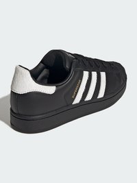 Czarny skórzany sneaker z białymi futrzanymi akcentami, wyposażony w trzy białe paski, teksturowany obcas i złote logo "SUPERSTAR".