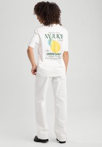 White t-shirt with a lemon graphic and text on the back, paired with loose-fitting white pants and black shoes. Smooth cotton texture.