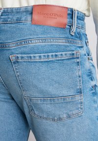 Jeans en denim bleu clair avec une poche arrière, ornés d'une étiquette en cuir marron embossée avec "Marc O'Polo" près de la taille.