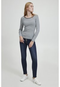 Blusa de manga larga a rayas con escote redondo, combinada con jeans oscuros ajustados con botones en la parte delantera y zapatillas blancas.