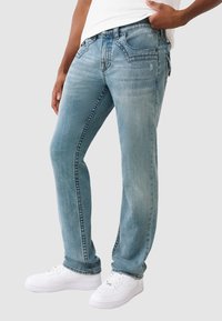 Jasnoniebieskie dżinsy z prostymi nogawkami, z delikatnym efektem wypłowienia i pięcioma kieszeniami. Połączone z białymi sneakersami.