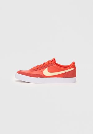 Red-orange sneakers with a soft fabric upper, featuring a white rubber sole and a prominent yellow Nike swoosh on the side.