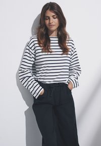 Top de manga larga con rayas horizontales en azul marino y blanco, cuello redondo, combinado con pantalones oscuros y holgados, con las manos en los bolsillos.