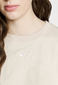 Beige sweatshirt i bomull med ribbad halsringning och ljusgrå broderad Nike-logotyp på bröstet. Mjuk textur, avslappnad design.