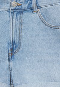 Jean en denim bleu clair à l'avant avec bouton métallique, fermeture éclair, passants de ceinture et détails de poches avant cousus.