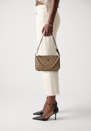 Pochette marron à motif avec une bandoulière en chaîne, de forme rectangulaire, en tissu texturé, et un détail en métal avec logo, tenue à côté d'un pantalon clair et de talons noirs.