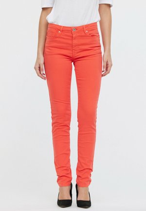 Jean skinny corail avec un design ajusté, cinq poches, fermeture à bouton à l'avant et texture lisse, associé à des escarpins noirs.