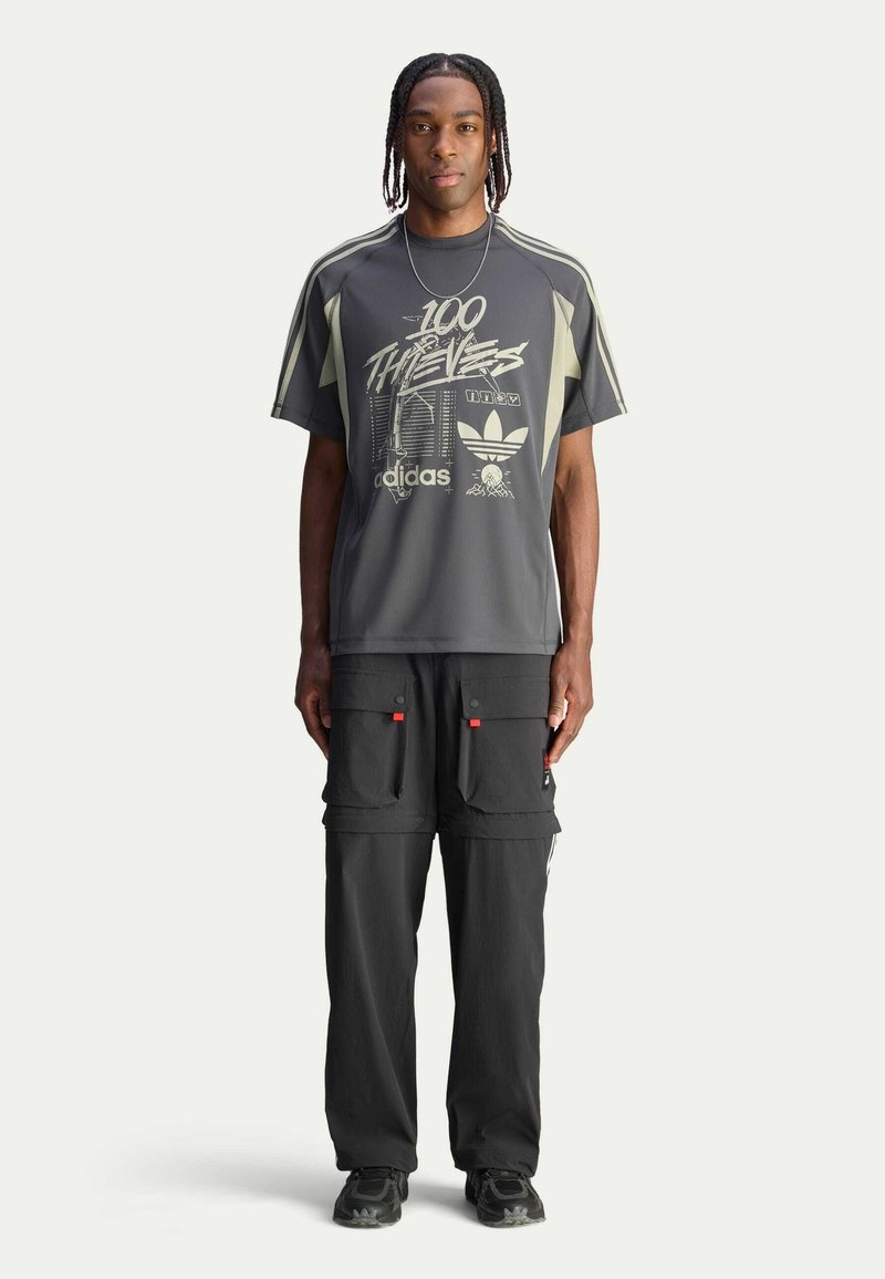 Grey athletic t-shirt with graphic print, short sleeves, and contrasting light green accents; paired with black cargo pants featuring pockets.