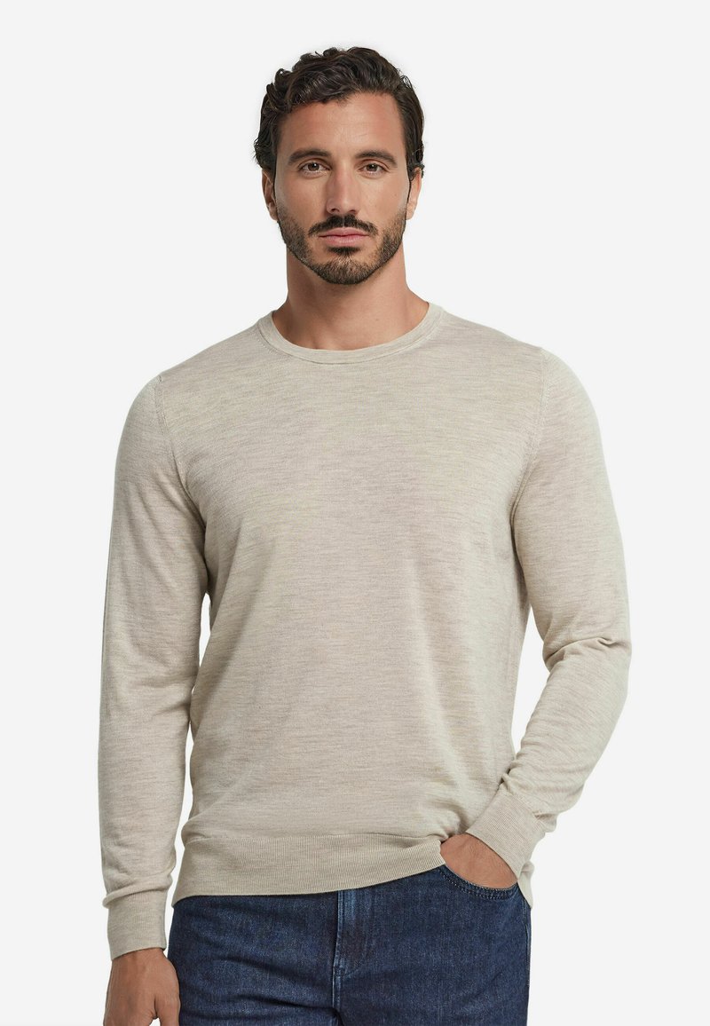 Heller beiger Pullover mit langen Ärmeln, Rundhalsausschnitt und gerippten Bündchen. Der Stoff wirkt weich und leicht strukturiert und wird mit dunklen Jeans kombiniert.