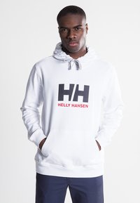 Sudadera blanca de mezcla de algodón, con un bolsillo delantero, capucha con cordón y un destacado logo "Helly Hansen" en negro y rojo.