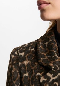 Cappotto di lana con stampa leopardata, caratterizzato da un colletto a punta e un tessuto texture in tonalità di marrone e nero, mostrando una vista ravvicinata senza il corpo intero.