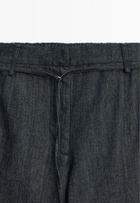 Donkerdenim broek met een rekbare tailleband, riemlussen en een gladde textuur. Kenmerken zijn subtiele stiksels en geen zichtbare zakken.