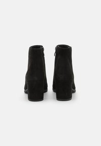 Schwarze Wildleder-Stiefeletten mit mattem Finish, die über einen Blockabsatz und einen seitlichen Reißverschluss verfügen. Glatte Textur mit strukturierter Form.