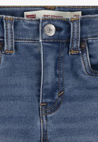 Jean droit Levi's 514 en denim bleu moyen, avec un bouton argenté, des coutures dorées contrastantes et des poches renforcées.