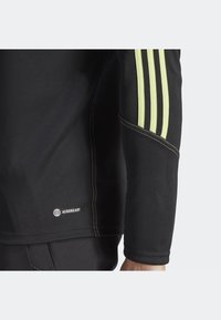 Black athletic jacket with long sleeves, featuring three yellow stripes on the shoulder, AEROREADY logo, and contrasting stitching.