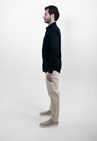 Zwarte longsleeve-shirt, beige chinos en beige instap schoenen, met een gladde textuur en slim fit, weergegeven in zijaanzicht op een witte achtergrond.