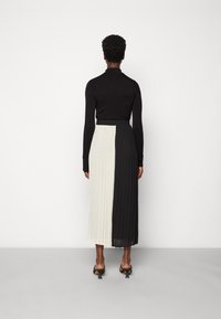 Gonna midi plissettata bianca e nera con vita elastica, abbinata a un top fitted a maniche lunghe nero; i tacchi aggiungono un'eleganza minimalista.