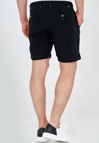 Shorts en jean noir avec un ourlet retroussé, dotés de poches arrière et d'accents de boutons. Associés à des baskets blanches et noires.