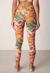 Legginsy w wielokolorowy wzór liści, z odcieniami zieleni, pomarańczu, różu i złota. Wykonane z elastycznego materiału, w wysoka talią.