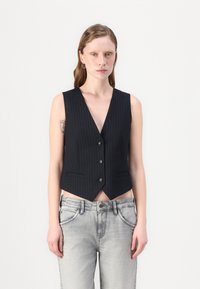 Schwarze Jersey-Weste mit feinen Streifen, tiefem V-Ausschnitt, vierknöpfigem Verschluss und zwei seitlichen Taschen, kombiniert mit grauen Jeans.